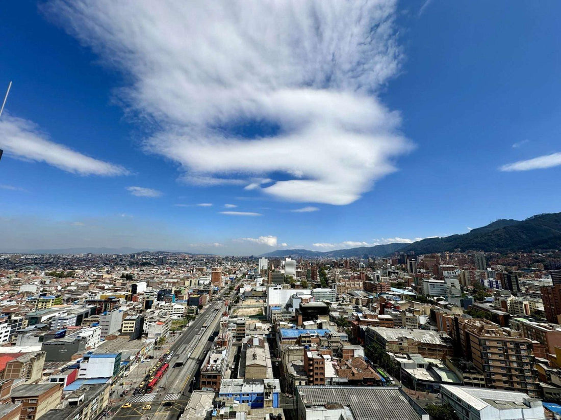 Aerial view of a densely built Bogota with a railway, surrounded by mountains under a blue sky