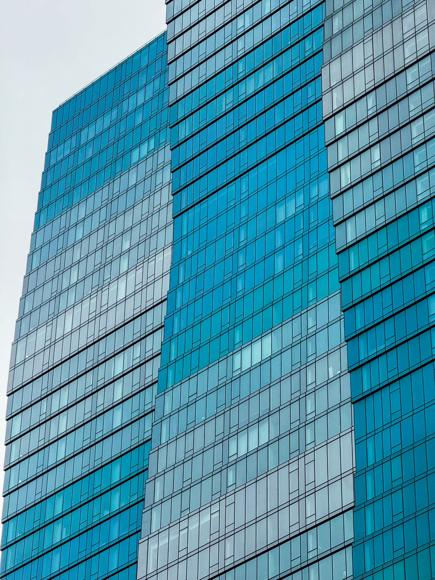 Close-up of Wavy Building - Fine Art Print captures contemporary glass skyscrapers with blue-tinted windows, highlighting geometric architectural art against a cloudy sky.