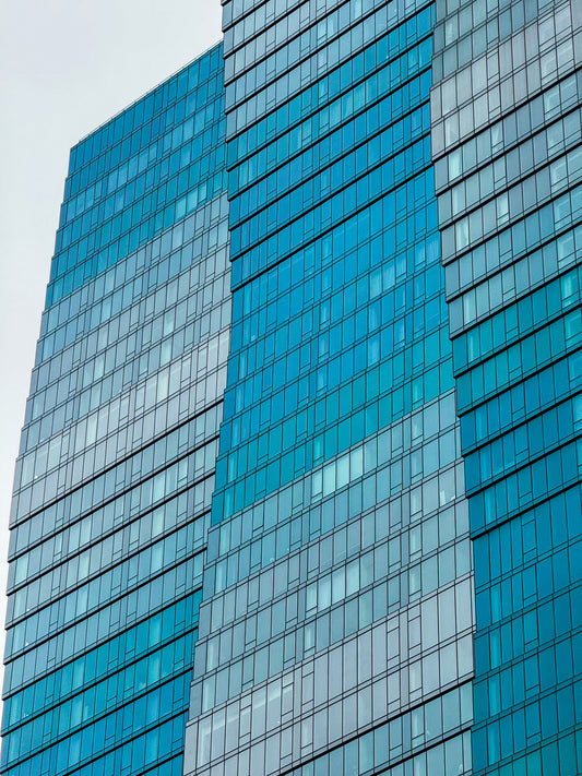 Close-up of Wavy Building - Fine Art Print captures contemporary glass skyscrapers with blue-tinted windows, highlighting geometric architectural art against a cloudy sky.