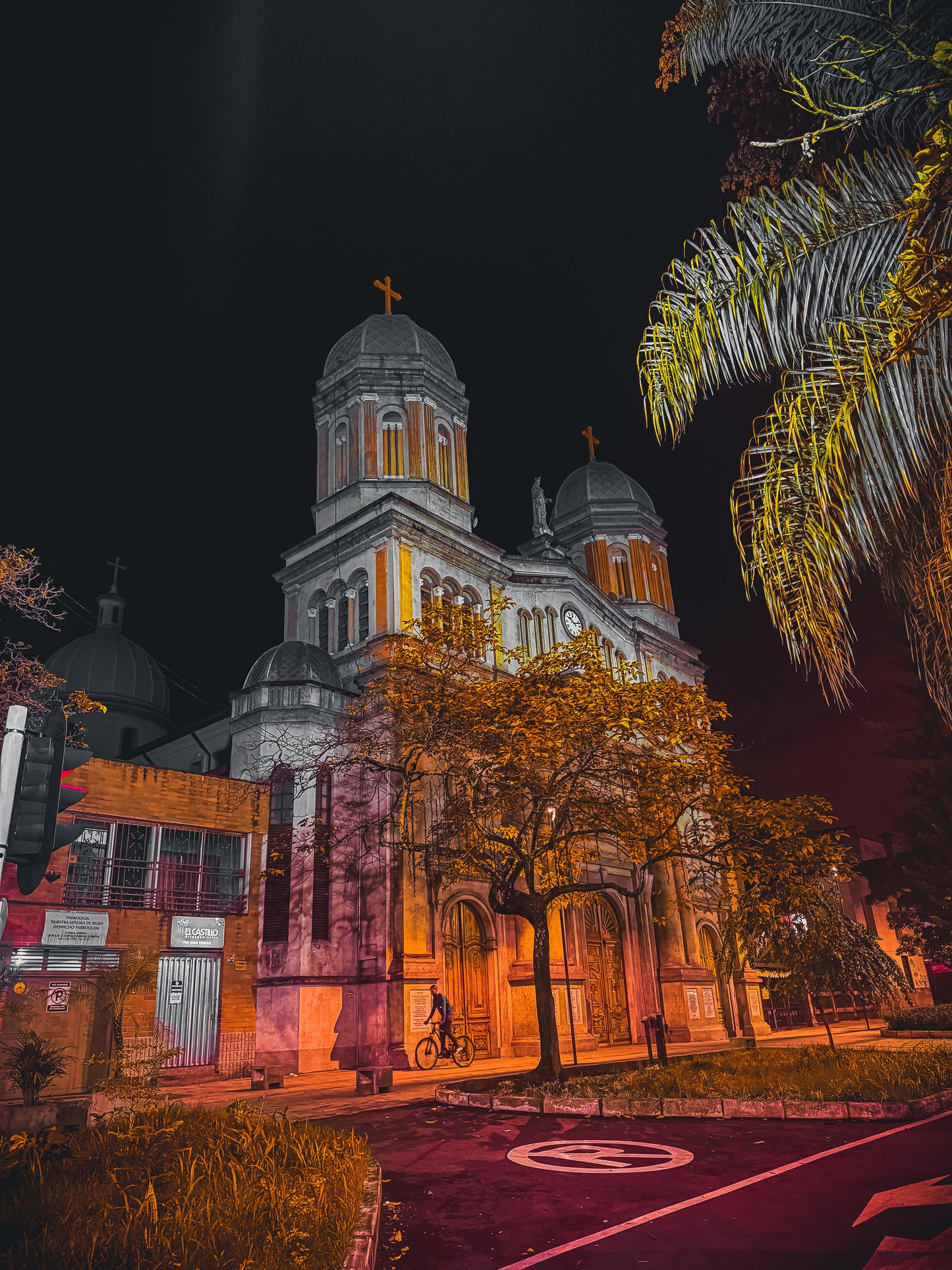 Church at Night - Fine Art Print by Leslie Brashear Photography captures a luminous church with domed towers behind a tree at night, as a cyclist passes in the foreground, evoking classic nighttime landscapes.