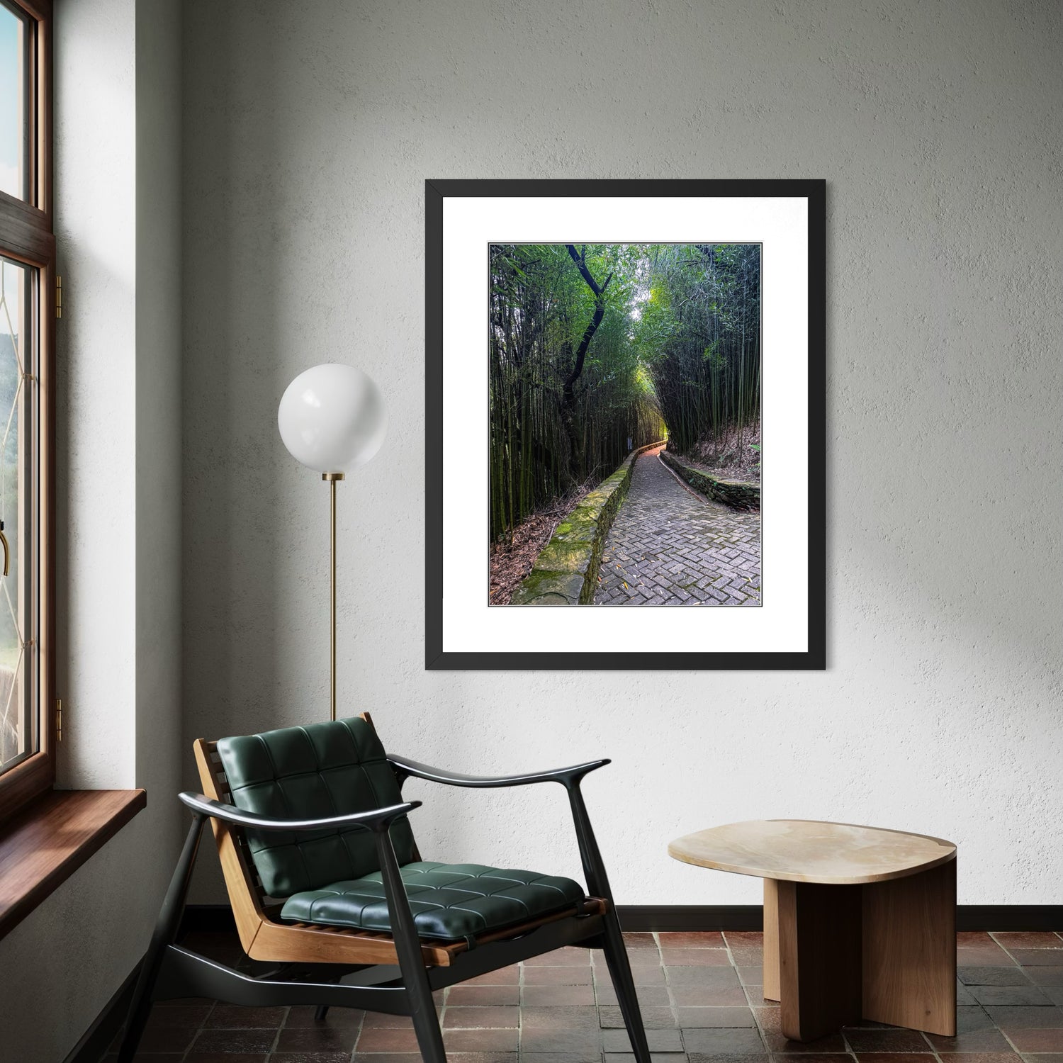 Framed artwork of a forest path on a wall above a chair and table.