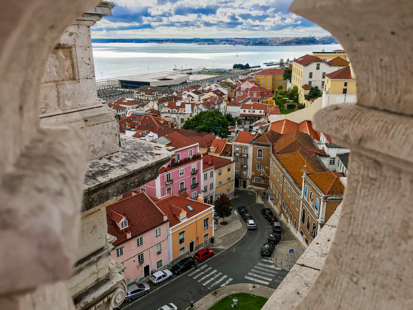 Lisbon - Fine Art Print: Captures a breathtaking Lisbon cityscape with red rooftops and narrow streets seen through a stone balustrade, with water and sky beyond—ideal for fans of Lisbon photography.